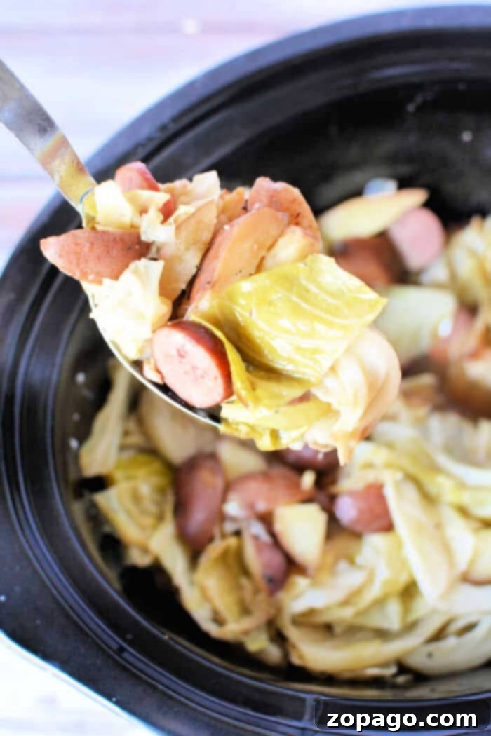 Effortless Slow Cooker Sausage Meals 5 A ladle scoops a portion of sliced sausages, chopped cabbage, and chunks of potatoes from a crockpot. The dish appears to be a hearty stew or casserole, perfectly illustrating classic crockpot sausage recipes with its delightful mix of meats and vegetables.