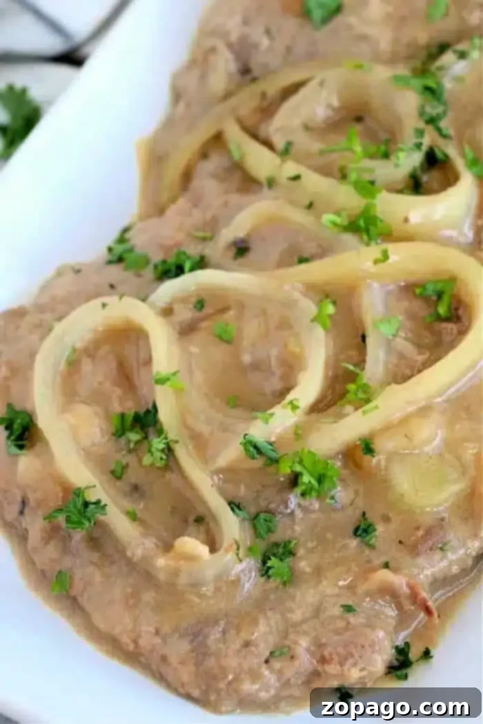 Delicious Minute Steaks in Savory Gravy 2 A close-up of a minute steak dish featuring succulent slices of meat covered in creamy sauce. Topped with crispy onion rings and garnished with chopped parsley, it's elegantly presented on a white plate.