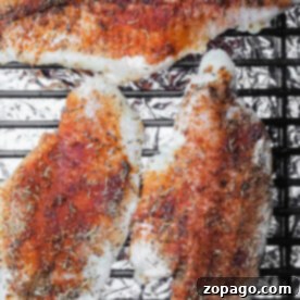 Three seasoned smoked catfish fillets sizzle enticingly on a grill, with foil underneath ensuring even cooking.