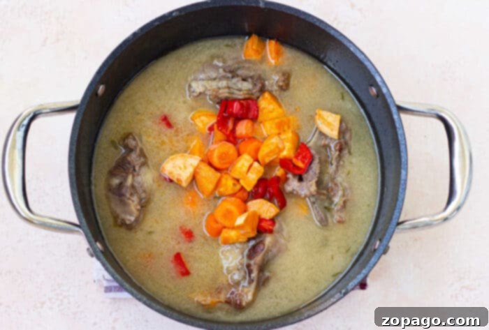 Braised Dutch Oven Oxtail 4 A pot of soup with tender beef ox tails, carrots, red peppers, and rich broth sits invitingly on a light background—a delightful hint for an easy oxtail recipe.