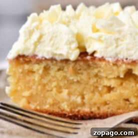 Close-up of a slice of moist lemon curd cake topped with whipped cream, placed on a plate with a fork nearby.