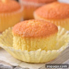 Golden lemon muffin recipe, one with an open wrapper, rest elegantly on a wooden board.