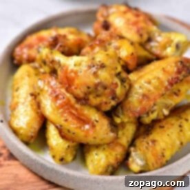 A plate of golden-brown air fryer honey lemon pepper wings is beautifully arranged on a wooden board. A small bowl of sauce sits invitingly in the background, complementing the savory delight.