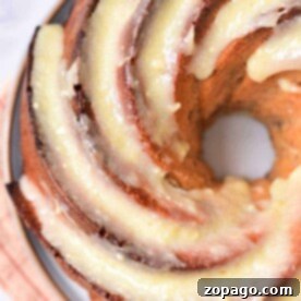 Close-up of a freshly baked bundt cake, glazed to perfection, on a plate with a striped cloth underneath—its the perfect Fresh Apple Cake Recipe in a Bundt Pan.