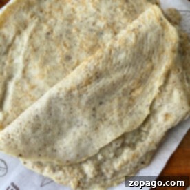 A stack of egg white tortillas sit elegantly on branded parchment paper atop a rustic wooden surface.