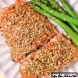 Almond crusted salmon fillets with asparagus rest elegantly on a white plate, placed on a cheerful yellow cloth.