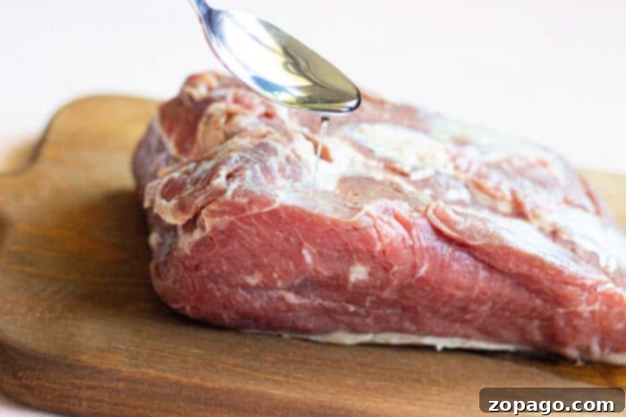 Mastering the New York Strip Roast 3 A spoon drizzling oil onto a raw piece of meat on a wooden cutting board sets the stage for mastering how to cook a New York Strip Roast.