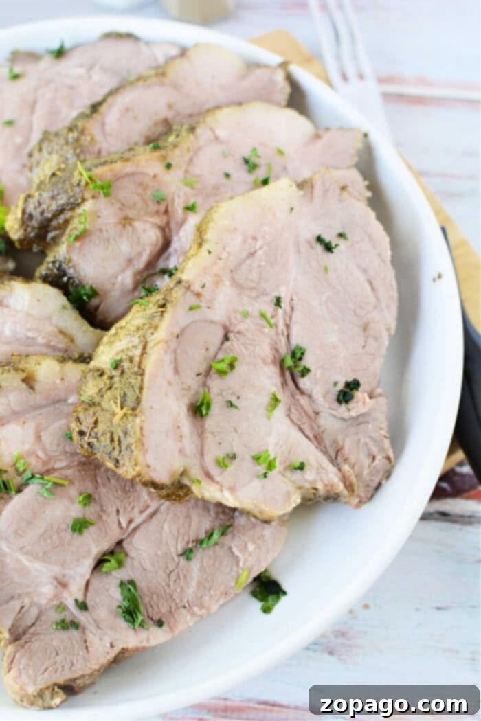 Tender Instant Pot Pork 2 Slices of seasoned tender pork roast, garnished with fresh parsley on a white plate, showcasing efficient pressure cooking results.