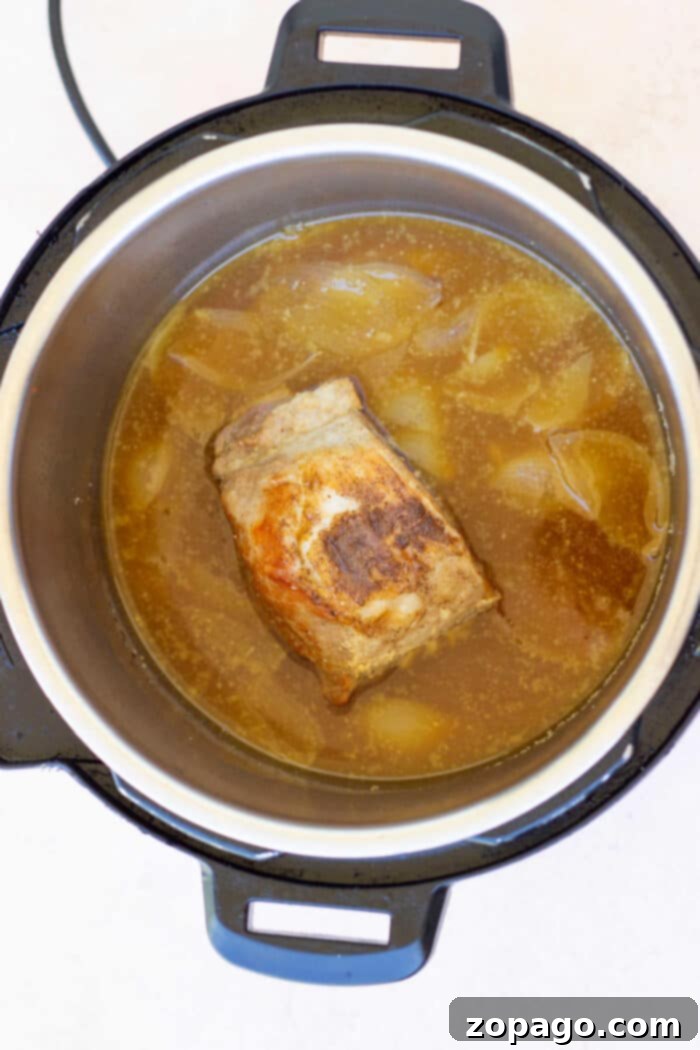 Tender Instant Pot Pork 7 A savory pork roast cooks to perfection in an Instant Pot, surrounded by chopped onions and simmering broth, ready for a delicious meal.