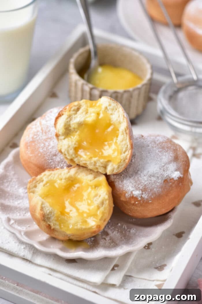 Zesty Lemon Burst Doughnuts 7 A top-down view of several lemon-filled donuts arranged on a white serving plate, dusted with powdered sugar, with a lemon slice garnish.