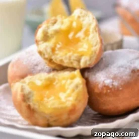 Zesty Lemon Burst Doughnuts 8 Close-up of air fryer lemon-filled donuts dusted with powdered sugar on a plate, with a glass of milk in the background.