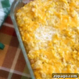 Homestyle Creamed Corn Bake 3 A rich, golden-brown cream corn casserole, topped with melted cheese, rests in a glass baking dish on a cozy plaid tablecloth.