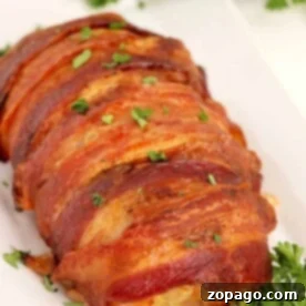 Meatloaf wrapped in crispy bacon, garnished with parsley, is elegantly served on a white plate with fresh herbs in the background.