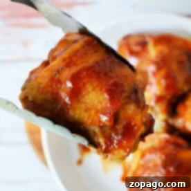 Easy Instant Pot BBQ Chicken Thighs 7 A close-up of an Instant Pot BBQ chicken thigh, perfectly grilled and held by tongs over a plate, with more glazed pieces tempting in the background.