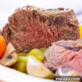 Close-up of a sliced Cross Rib Roast with tender carrots, potatoes, and mushrooms on a plate.