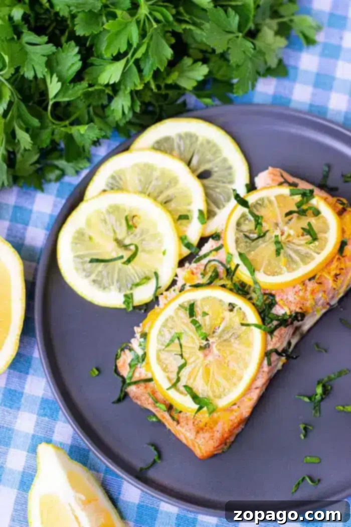 Perfect Baked Salmon Timing at 350 Degrees 2 A plate containing a piece of cooked salmon topped with lemon slices and chopped green herbs, ready to be served.