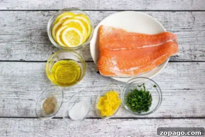 Perfect Baked Salmon Timing at 350 Degrees 3 A plate with raw salmon fillets, surrounded by small bowls containing lemon slices, olive oil, black pepper, salt, lemon zest, and chopped herbs, all placed on a white wooden surface, preparing for seasoning.
