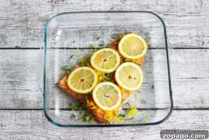 Perfect Baked Salmon Timing at 350 Degrees 5 A glass baking dish contains a piece of salmon fillet topped with lemon slices and herbs, freshly baked and ready to serve.