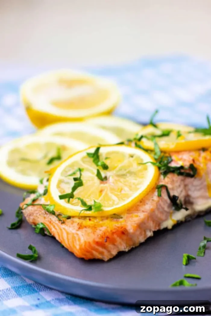 Perfect Baked Salmon Timing at 350 Degrees 6 A piece of baked salmon garnished with lemon slices and chopped herbs is on a dark plate, highlighting its perfect cook.