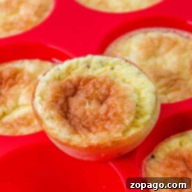 Close-up of crustless mini quiche muffins in a red silicone baking tray, one muffin slightly raised above the others.