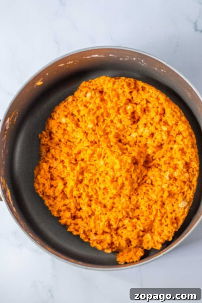 Crispy Autumn Pumpkin Bites 4 A large non-stick pan filled with bright orange marshmallow cereal treats, a vibrant base for Halloween Rice Krispie Treats, set on a clean marble surface.