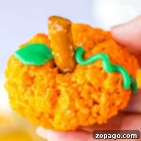 A single, perfectly crafted orange Rice Krispie treat shaped like a pumpkin, adorned with a pretzel stick stem and a green Airhead leaf and vine.