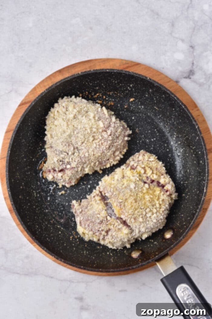 Tenderized Venison Steak 6 Two breaded venison steaks are sizzling in a non-stick frying pan on a marble surface, creating a delicious venison cube steak recipe.