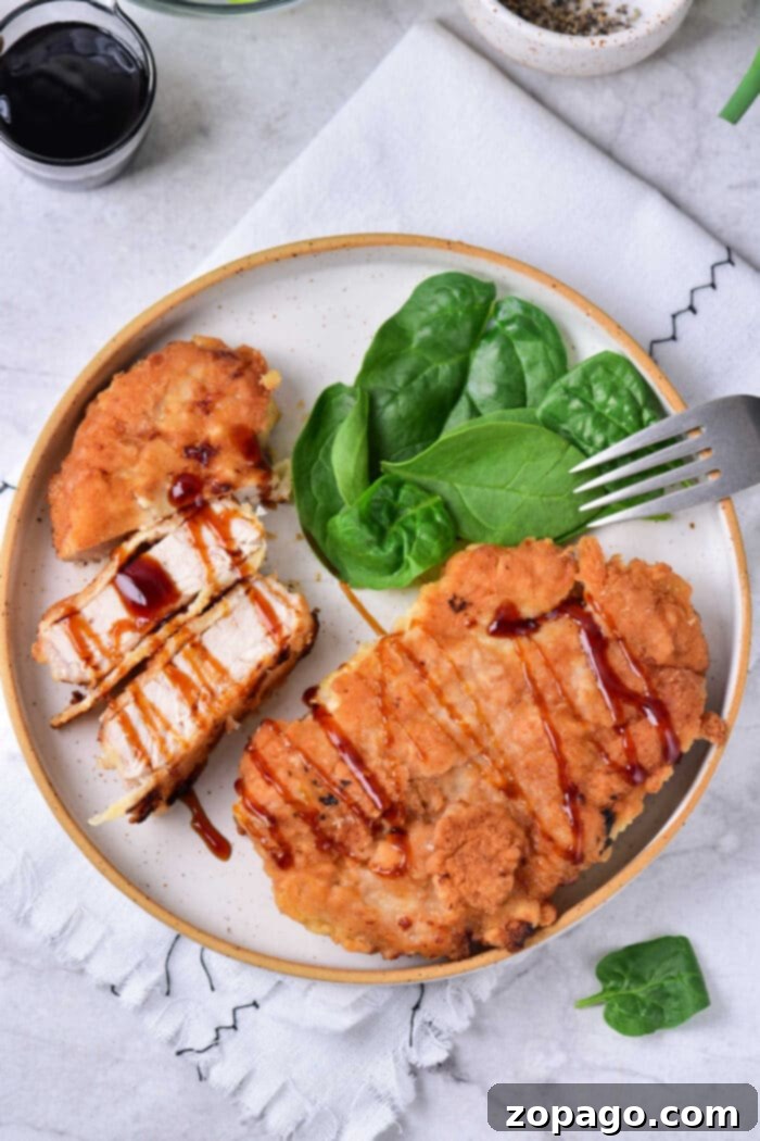 Pork Cutlets 6 Fried pork cube steak drizzled with barbecue sauce rest alongside fresh spinach and a fork on a plate.