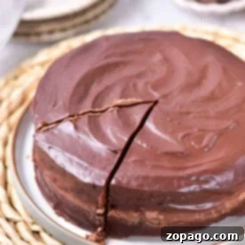 Chocolate coffee cake with a shiny ganache frosting and one slice cut out, resting on a woven placemat.