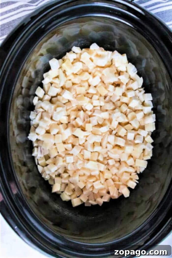 Perfectly Crispy Frozen Hash Browns 4 Diced frozen potatoes inside a slow cooker on a striped cloth backdrop, offering a hint of how to cook frozen hash browns with ease.