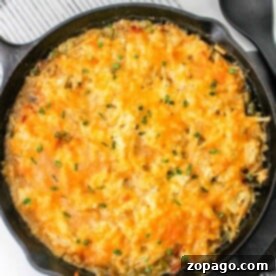Hash brown casserole without soup in a cast iron skillet rests on a striped placemat, with a black serving spoon nearby.