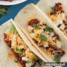 Three chorizo tacos with cheese, onion, and cilantro are delightfully served on a blue plate.