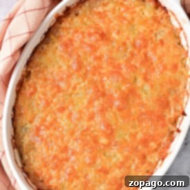 Golden-brown Ground Beef Hash Brown casserole in a white dish on a plaid cloth, with a spoonful ready to serve.