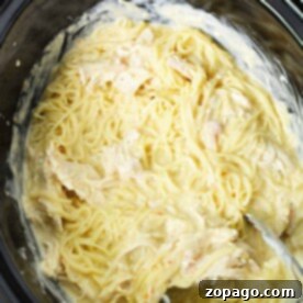 Heavenly Creamy Slow Cooker Chicken 6 Angel Crockpot Chicken: Creamy pasta with shredded chicken in a black slow cooker, elegantly served with metal tongs.