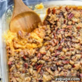 A glass dish with a delectable sweet potato casserole recipe featuring canned yams, topped with crunchy pecans and accompanied by a wooden spoon.