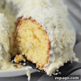 White Chocolate Coconut Bundt Bliss 7 A slice of moist white chocolate coconut bundt cake with creamy white frosting and shredded coconut on a spatula, ready to be served.