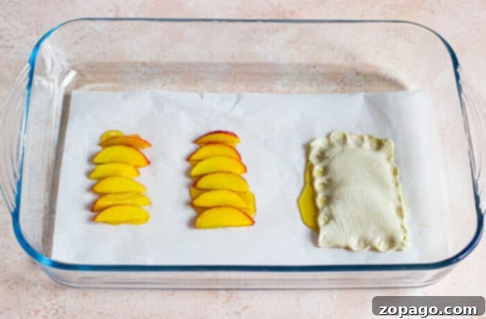 Individual peach tarts with puff pastry arranged on a baking sheet.