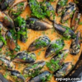 Curry Mussels simmer in a creamy, spiced sauce topped with fresh herbs in a pan.