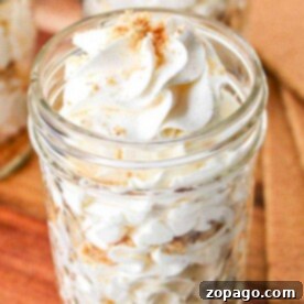 A jar filled with layers of cool whip frosting, crumbs, and a silky cream cheese frosting without butter, topped with more whipped cream and crumbs on a wooden surface.