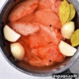 A pot filled with chicken wings, bay leaves, onion halves, and a blend of spices gently simmering in broth.