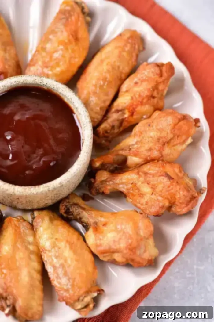 Poached Chicken Wings 6 A plate of golden-brown, boiled chicken wings is arranged in a circular pattern around a small bowl filled with dark barbecue sauce. The plate rests elegantly on an orange cloth.