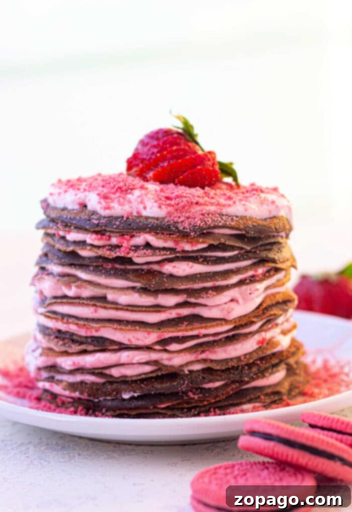 A stack of chocolate crepes layered with pink cream, topped with a strawberry on a white plate, offers an effortless treat reminiscent of learning how to make crepes with pancake mix for elegant brunches.