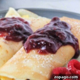 Savory crepes with raspberry jam and powdered sugar on a plate, alongside fresh raspberries, offering a delightful twist on classic ham and cheese crepes.