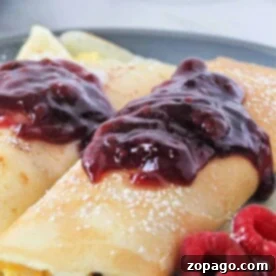 Crepes topped with raspberry jam and powdered sugar, served with fresh raspberries on a plate, can be delightfully versatile, just like ham and cheese crepes, offering a savory twist to the classic dish.