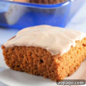 A slice of frosted pumpkin cake, reminiscent of a classic Crazy Cake, rests on a white plate with a vibrant blue dish in the background.