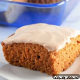 A slice of frosted pumpkin cake, reminiscent of a classic Crazy Cake, rests on a white plate with a vibrant blue dish in the background.