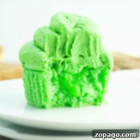 A vibrant green cupcake with frosting rests elegantly on a white plate, delighting those with a penchant for green cupcakes.