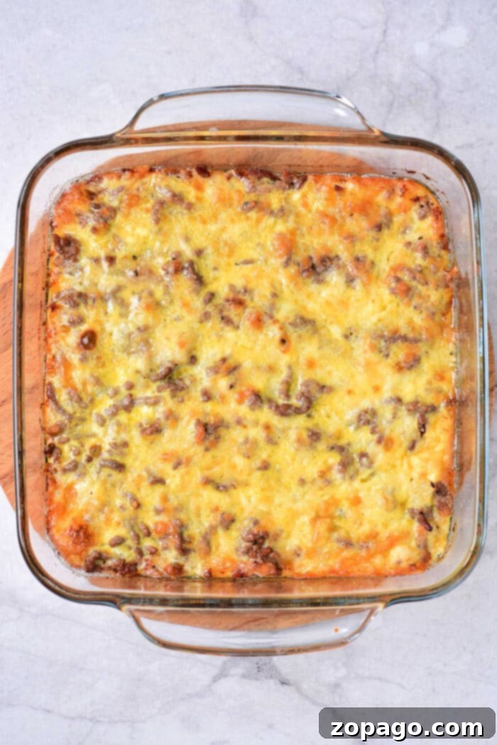 Special Sauce Cheeseburger Casserole 4 A Big Mac Casserole with a golden-brown cheese topping sits in a clear glass baking dish. The casserole, featuring ground meat and layers of melty cheese, boasts a slightly crispy surface. It rests invitingly on a white marble countertop, promising classic flavors in every bite.