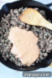 Big Mac Bake 8 Ground beef simmered in a creamy, Big Mac-inspired sauce, mingling with sautéed onions in a skillet. A wooden spatula rests nearby, ready to serve these delightful Sloppy Joes.