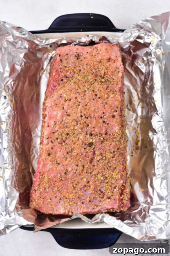 The Ultimate Corned Beef Stack 4 Seasoned with aromatic spices, a raw corned beef roast awaits its transformation into a delectable sandwich centerpiece, nestled in a foil-lined baking dish for optimal roasting.